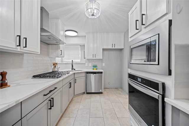 kitchen featuring stainless steel appliances, a sink, wall chimney range hood, backsplash, and light stone countertops