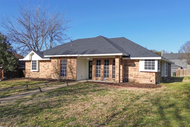 back of property featuring brick siding, a lawn, and a shingled roof