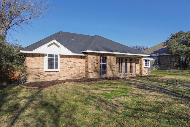 rear view of property with a shingled roof, brick siding, and a yard