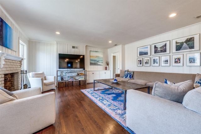 living room featuring dark wood-style floors, a brick fireplace, visible vents, and crown molding