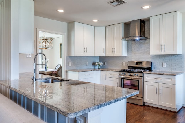 kitchen featuring light stone counters, visible vents, stainless steel gas stove, a sink, and wall chimney exhaust hood