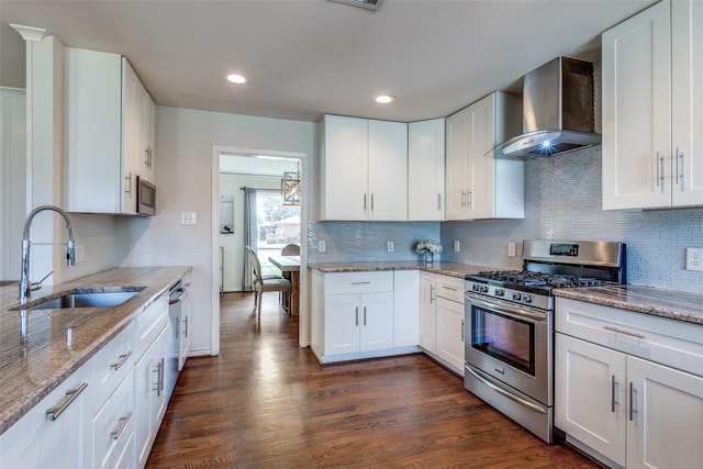 kitchen with stainless steel appliances, dark wood-style flooring, a sink, and wall chimney range hood