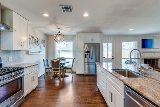 kitchen with visible vents, dark wood finished floors, appliances with stainless steel finishes, wall chimney range hood, and a sink