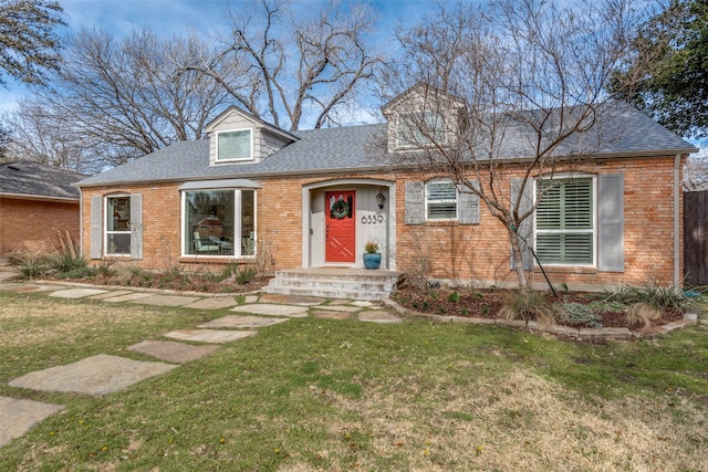 view of front of home with a shingled roof, brick siding, and a front lawn