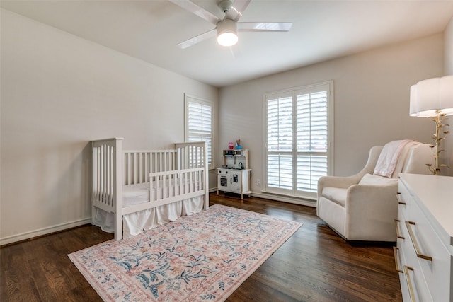 bedroom featuring a ceiling fan, dark wood-style flooring, a crib, and baseboards