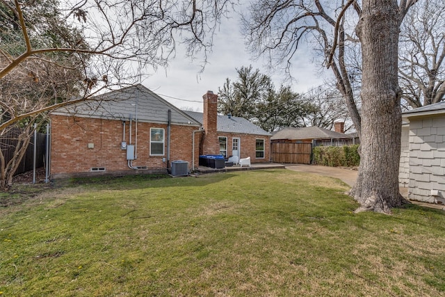 rear view of house featuring central air condition unit, brick siding, fence, a yard, and a chimney