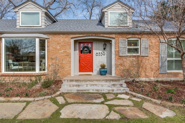 entrance to property with a shingled roof and brick siding