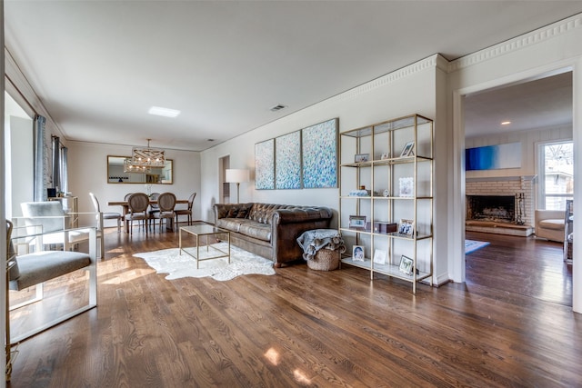 living area featuring a brick fireplace, visible vents, ornamental molding, and wood finished floors