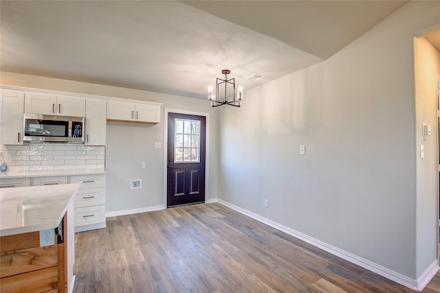 kitchen featuring light wood finished floors, tasteful backsplash, stainless steel microwave, white cabinetry, and baseboards