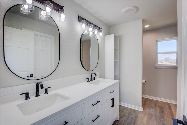 full bath featuring double vanity, wood finished floors, a sink, and baseboards