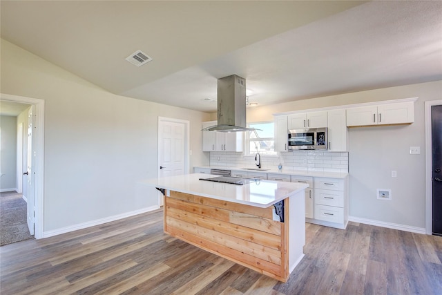 kitchen with island range hood, visible vents, a kitchen island, stainless steel microwave, and white cabinetry