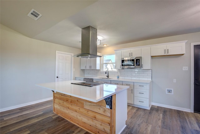 kitchen featuring island range hood, visible vents, stainless steel microwave, a center island, and backsplash