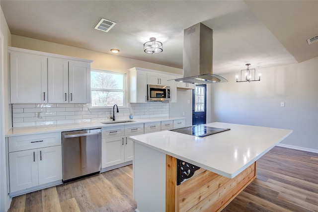 kitchen with island exhaust hood, visible vents, backsplash, appliances with stainless steel finishes, and a sink