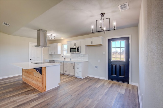 kitchen featuring stainless steel microwave, a sink, visible vents, and island range hood