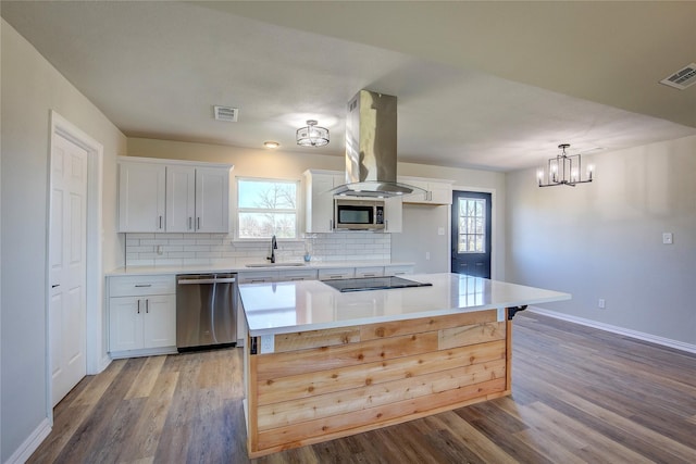 kitchen featuring visible vents, decorative backsplash, island exhaust hood, stainless steel appliances, and white cabinetry