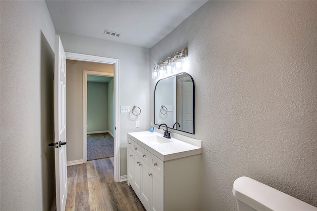 half bathroom featuring baseboards, visible vents, toilet, wood finished floors, and vanity