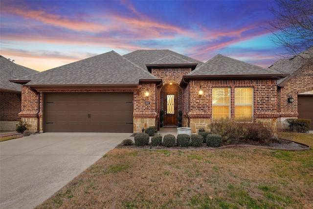 french country home featuring brick siding, a shingled roof, a garage, driveway, and a front lawn