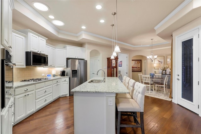 kitchen featuring arched walkways, appliances with stainless steel finishes, dark wood-type flooring, a tray ceiling, and a sink