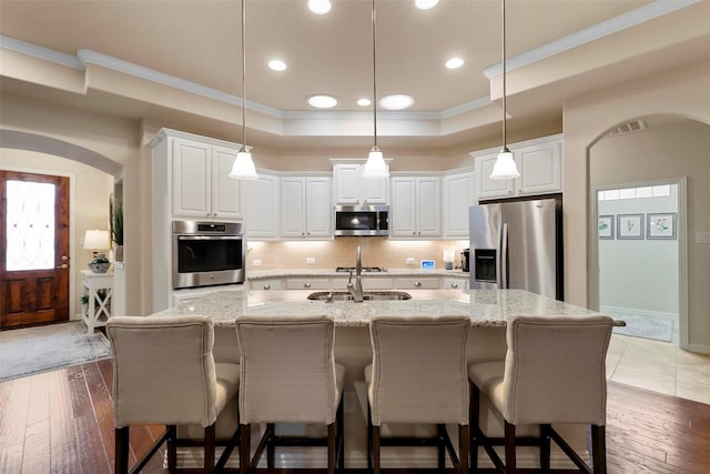 kitchen with arched walkways, a raised ceiling, appliances with stainless steel finishes, crown molding, and backsplash