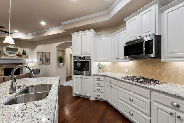 kitchen with arched walkways, ornamental molding, dark wood-style flooring, stainless steel appliances, and a sink