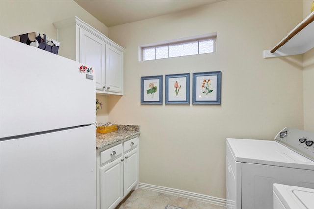 clothes washing area featuring washing machine and dryer, cabinet space, and baseboards