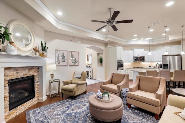 living area featuring visible vents, arched walkways, dark wood finished floors, a tray ceiling, and crown molding