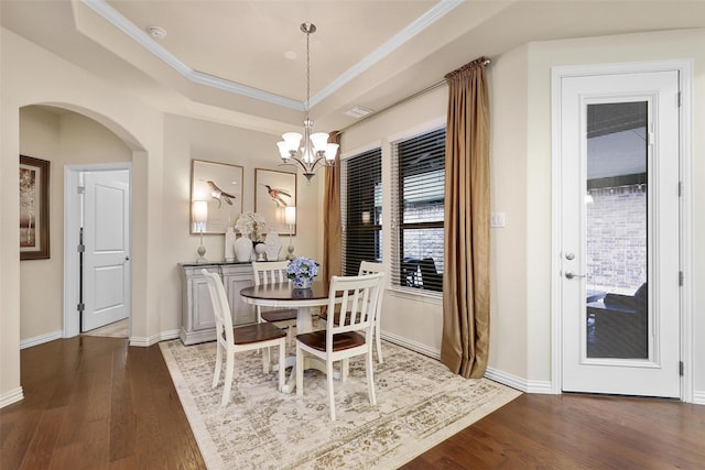 dining area with arched walkways, a raised ceiling, baseboards, and wood finished floors