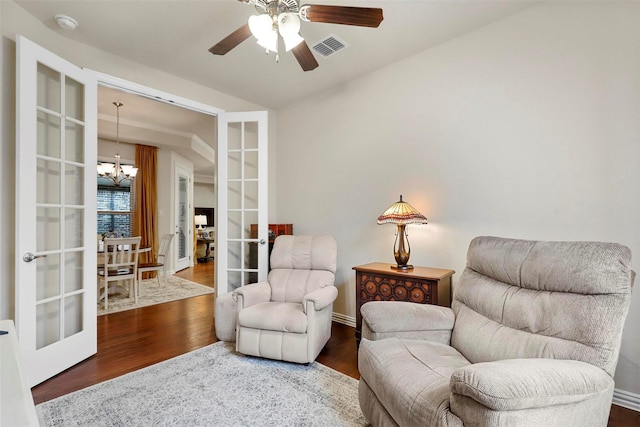 sitting room with ceiling fan with notable chandelier, french doors, wood finished floors, and visible vents