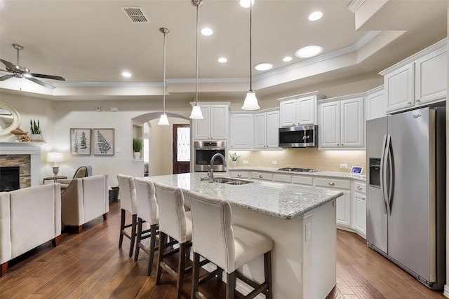 kitchen with arched walkways, a raised ceiling, appliances with stainless steel finishes, open floor plan, and a sink