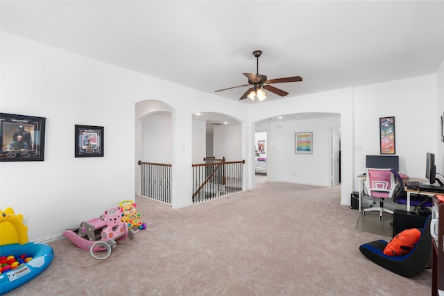 rec room with ceiling fan, carpet, arched walkways, and a desk