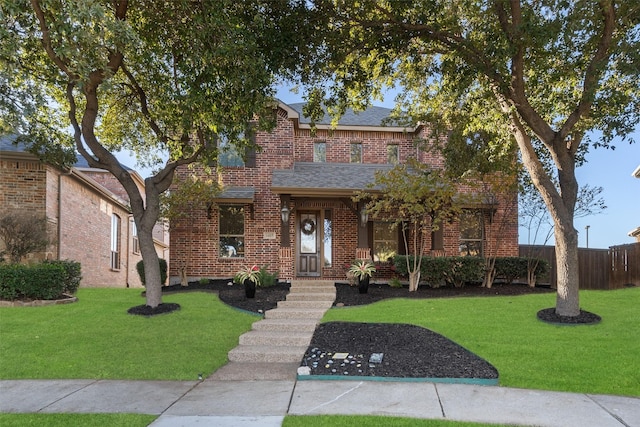 traditional-style home with brick siding, a front yard, fence, and a shingled roof