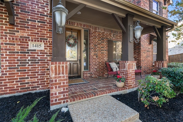 view of exterior entry with brick siding and a porch