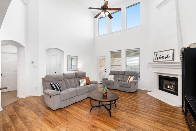 living area with arched walkways, ceiling fan, a towering ceiling, a fireplace, and wood finished floors