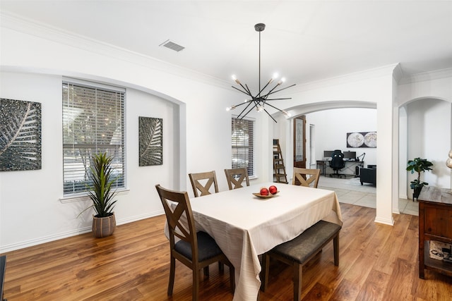 dining space featuring arched walkways, a chandelier, wood finished floors, ornamental molding, and baseboards