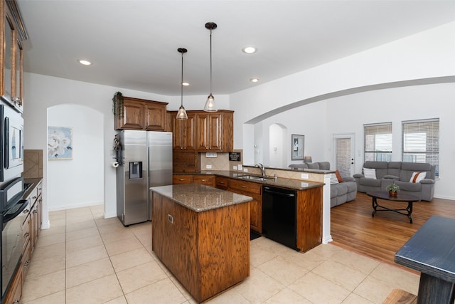 kitchen featuring arched walkways, a sink, open floor plan, a center island, and black appliances