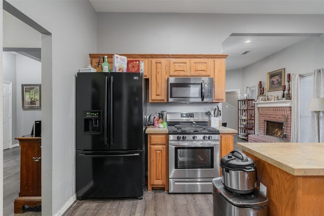 kitchen featuring stainless steel appliances, a fireplace, wood finished floors, baseboards, and light countertops