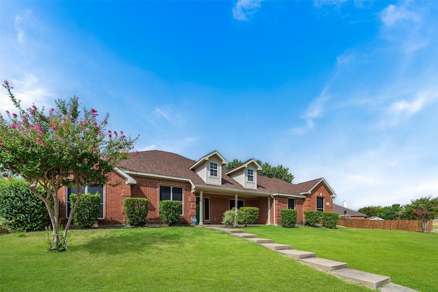 view of front of property featuring a shingled roof, a front yard, fence, and brick siding