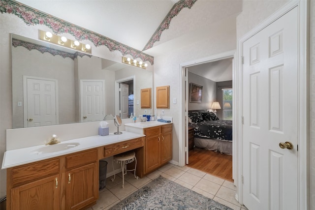 ensuite bathroom with double vanity, lofted ceiling, ensuite bathroom, a sink, and tile patterned flooring