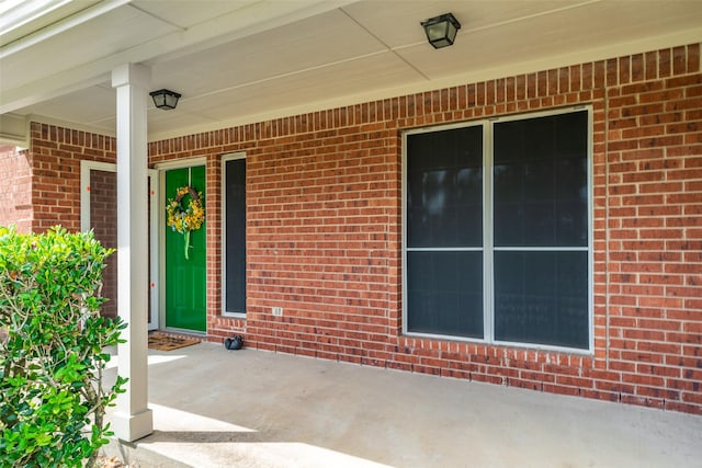 view of exterior entry with covered porch and brick siding