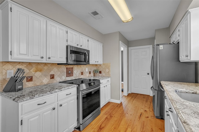 kitchen featuring tasteful backsplash, visible vents, white cabinets, stainless steel appliances, and light wood-style floors