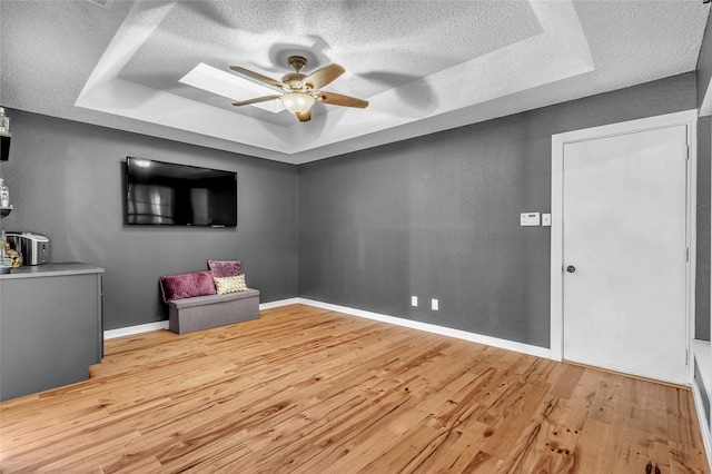 interior space with a textured ceiling, a tray ceiling, light wood-type flooring, and a ceiling fan