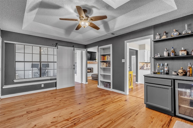 bar featuring a barn door, wine cooler, light wood-type flooring, a dry bar, and a raised ceiling