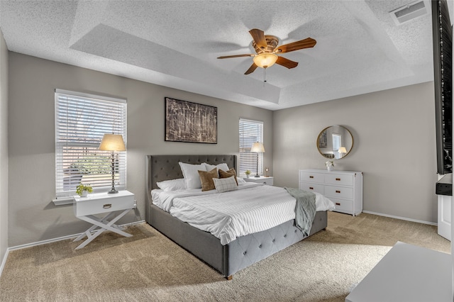 bedroom with carpet floors, multiple windows, a tray ceiling, and a textured ceiling