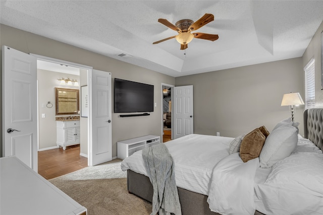 bedroom with a raised ceiling, visible vents, a textured ceiling, and ensuite bath