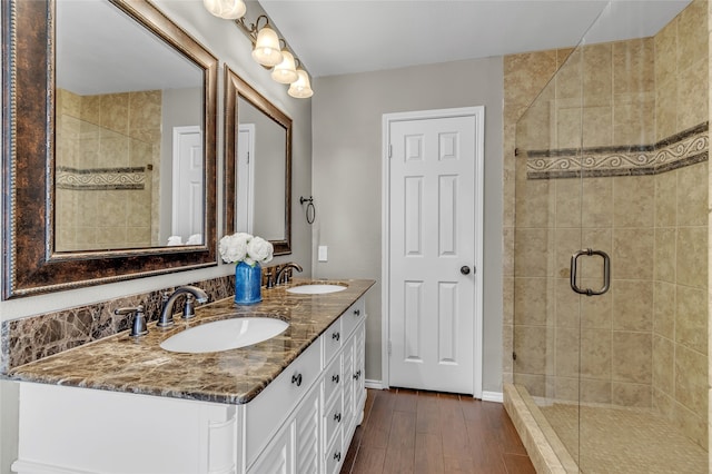 bathroom with double vanity, a shower stall, a sink, and wood finished floors