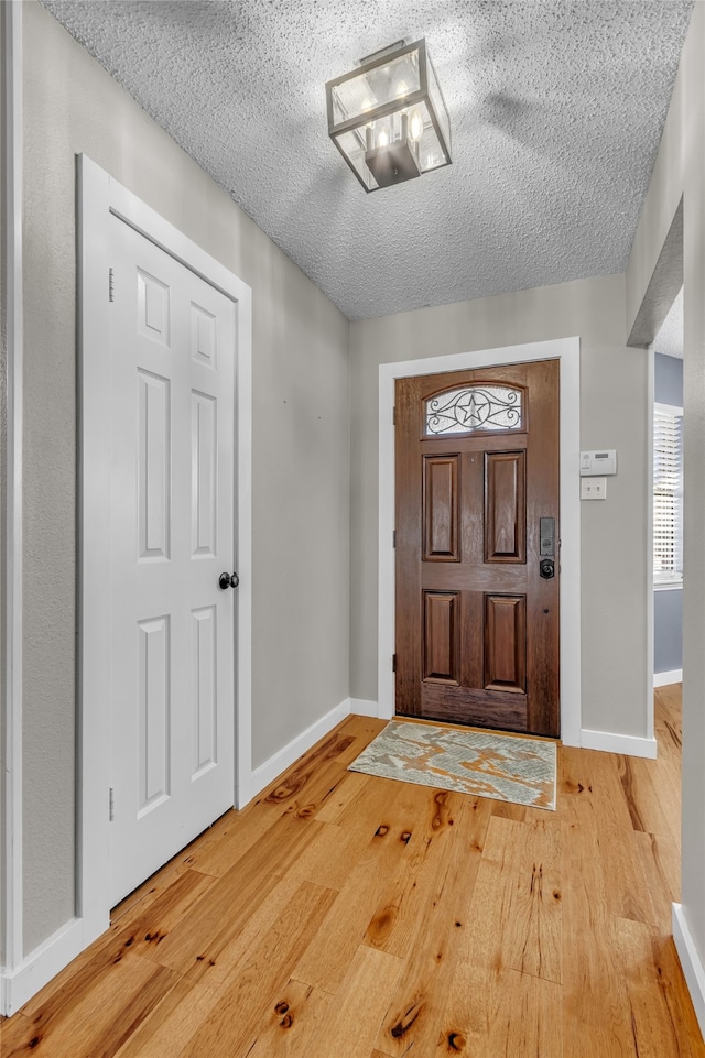 entryway with a textured ceiling, light wood-style flooring, and baseboards