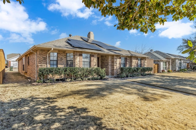 ranch-style home featuring brick siding, a chimney, and solar panels