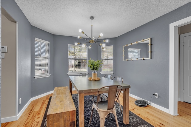 dining space with a textured ceiling, light wood-type flooring, baseboards, and an inviting chandelier