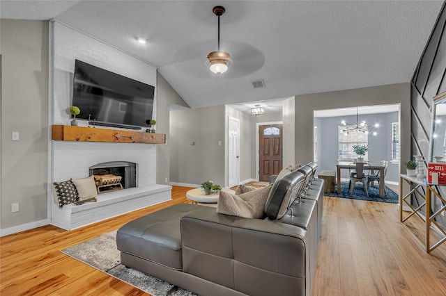 living area with visible vents, baseboards, wood-type flooring, vaulted ceiling, and a brick fireplace