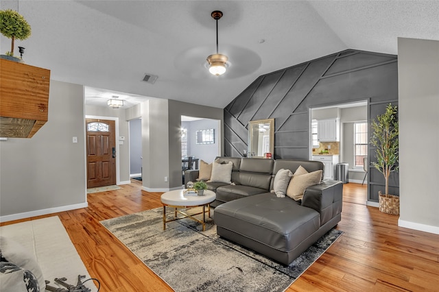 living area featuring lofted ceiling, a textured ceiling, visible vents, baseboards, and light wood-type flooring